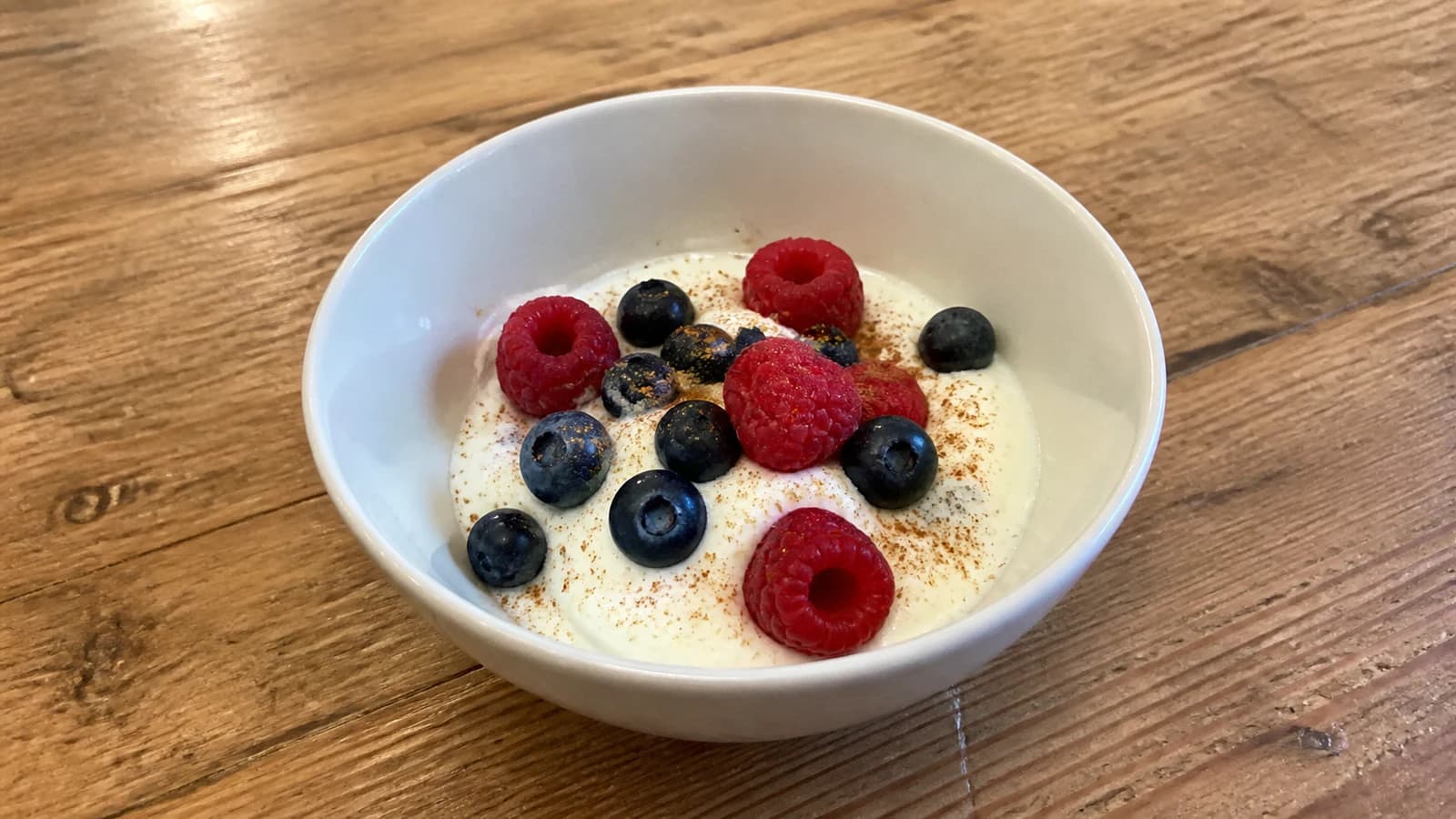 Small bowl of plain Greek yogurt with blueberries, raspberries, and a light dusting of cinnamon